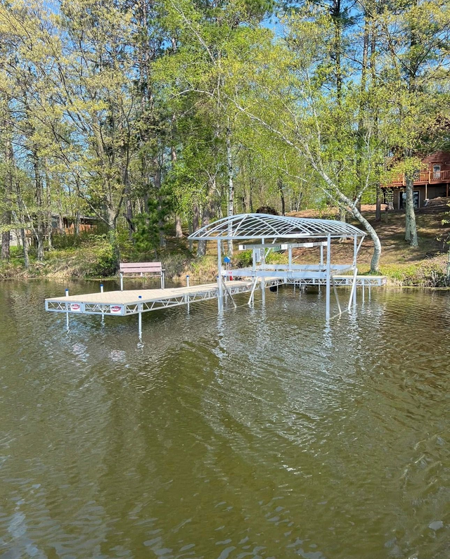 Lakefront cabin with dock and covered boat lift, reflected in calm water surrounded by trees.