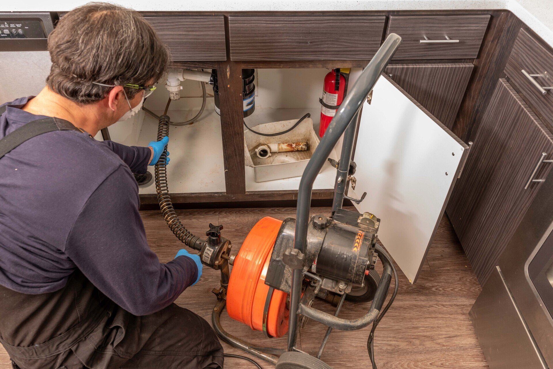 Professional plumber using an auger to clear a kitchen sink drain - Sanford MI