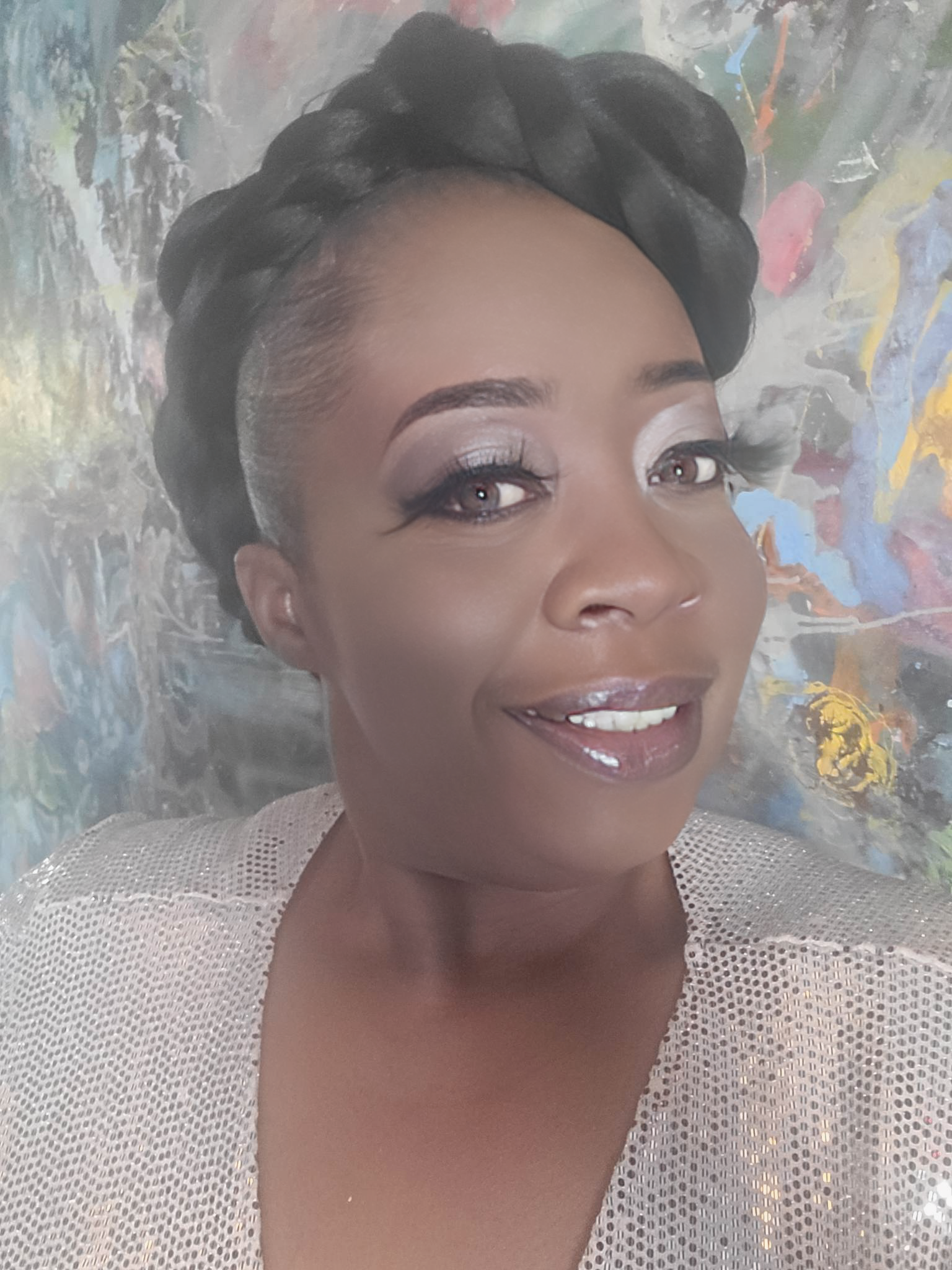A woman with a braided headband is smiling in front of a painting.