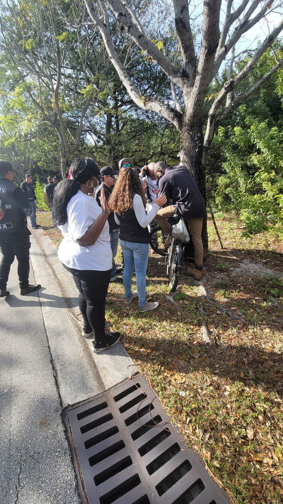 A group of people are standing on the side of a road next to a tree.