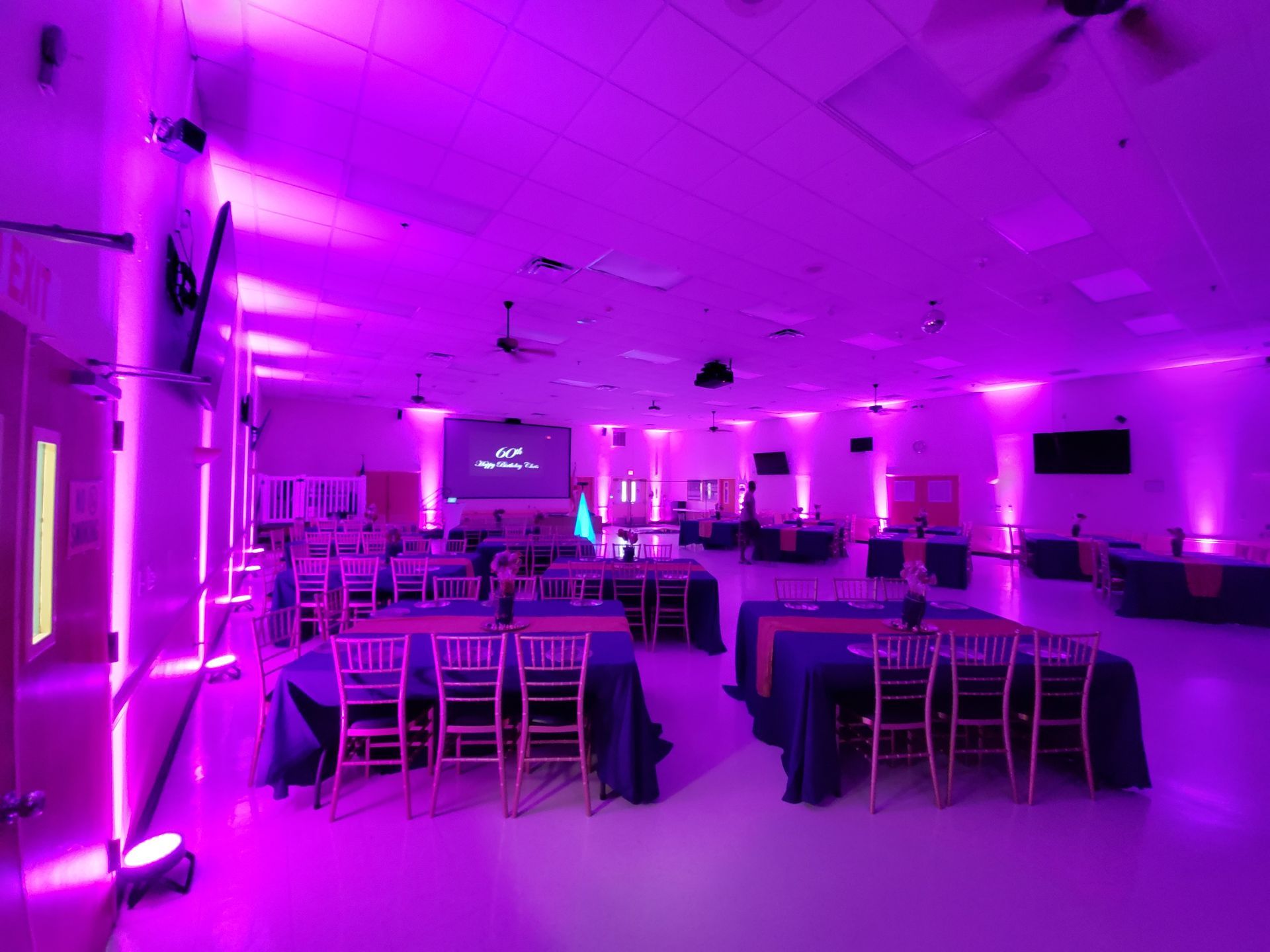 Empty banquet hall with tables and chairs lit by vivid purple ambient lighting
