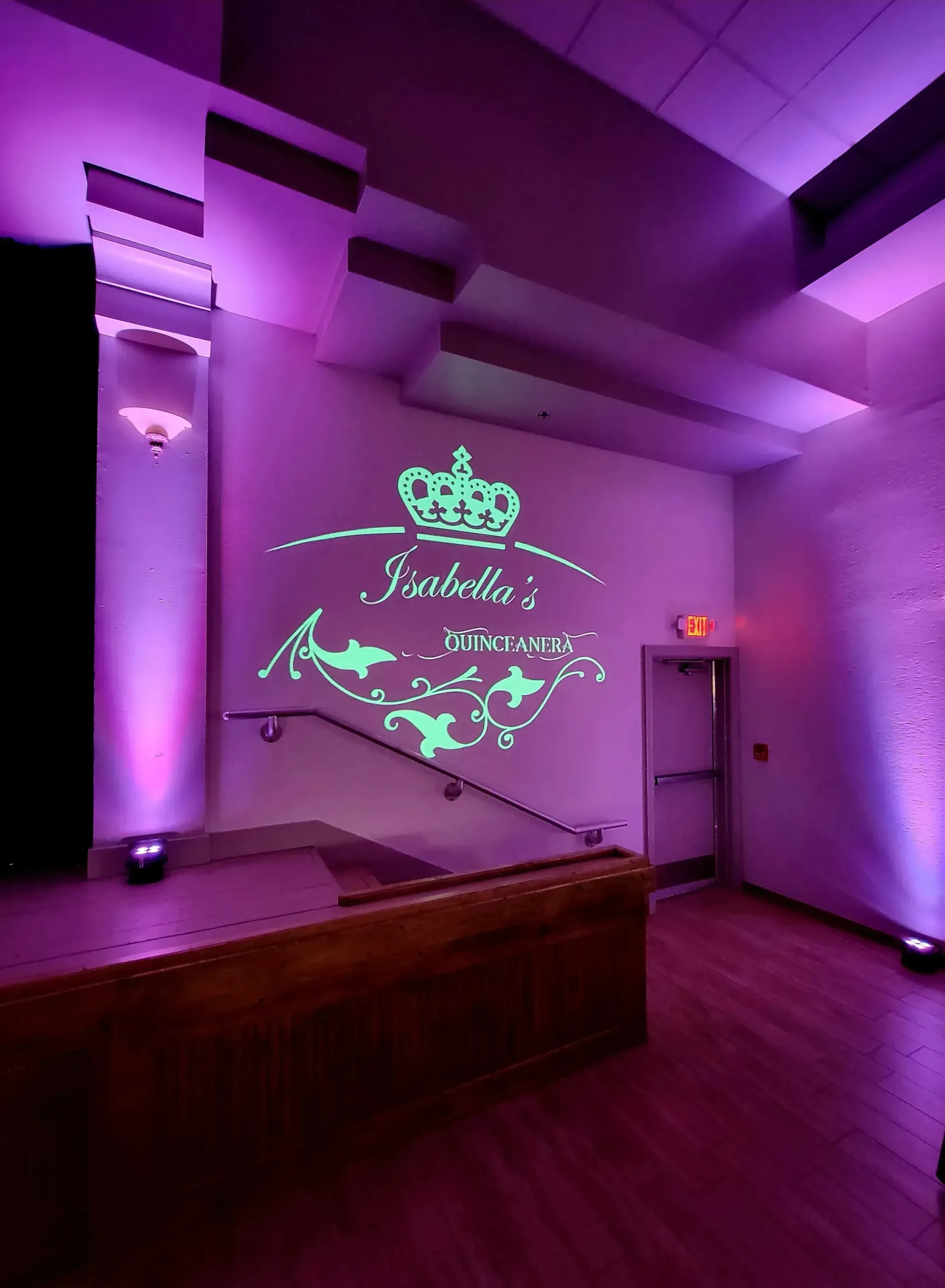 Purple-lit event room with a neon anniversary-style sign on a wall above a small stage