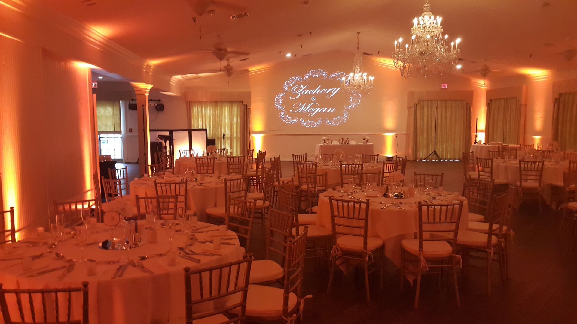 Elegant banquet hall with warm orange lighting, chandeliers, and rows of empty chairs and tables