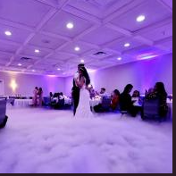 Bride in a white dress and veil stands on a cloud-like floor in a purple-lit wedding reception hall.