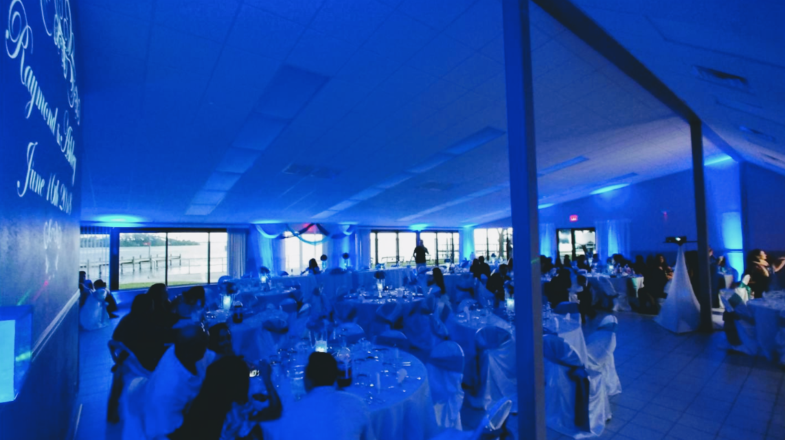 Blue-lit banquet tent with round tables, seated guests, and a stage at the far end