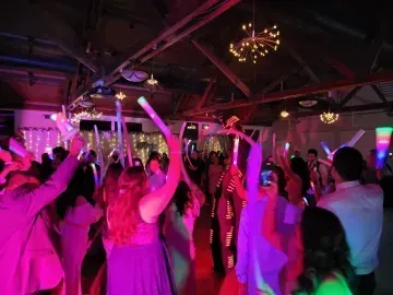 Crowded dance floor lit pink and purple, people raising their arms under chandeliers in a party venue