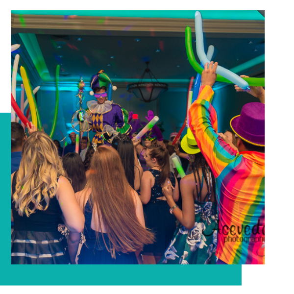 Crowd at a colorful indoor party waving balloon tubes toward a performer on stage
