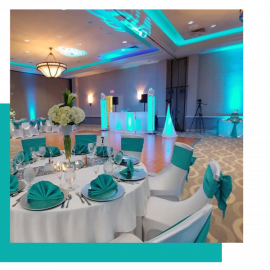 Elegant banquet hall with teal-lit stage and round tables set with white tablecloths and teal napkins