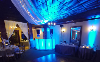 Blue-lit event venue with draped ceiling, glowing bar, and set tables for a formal reception