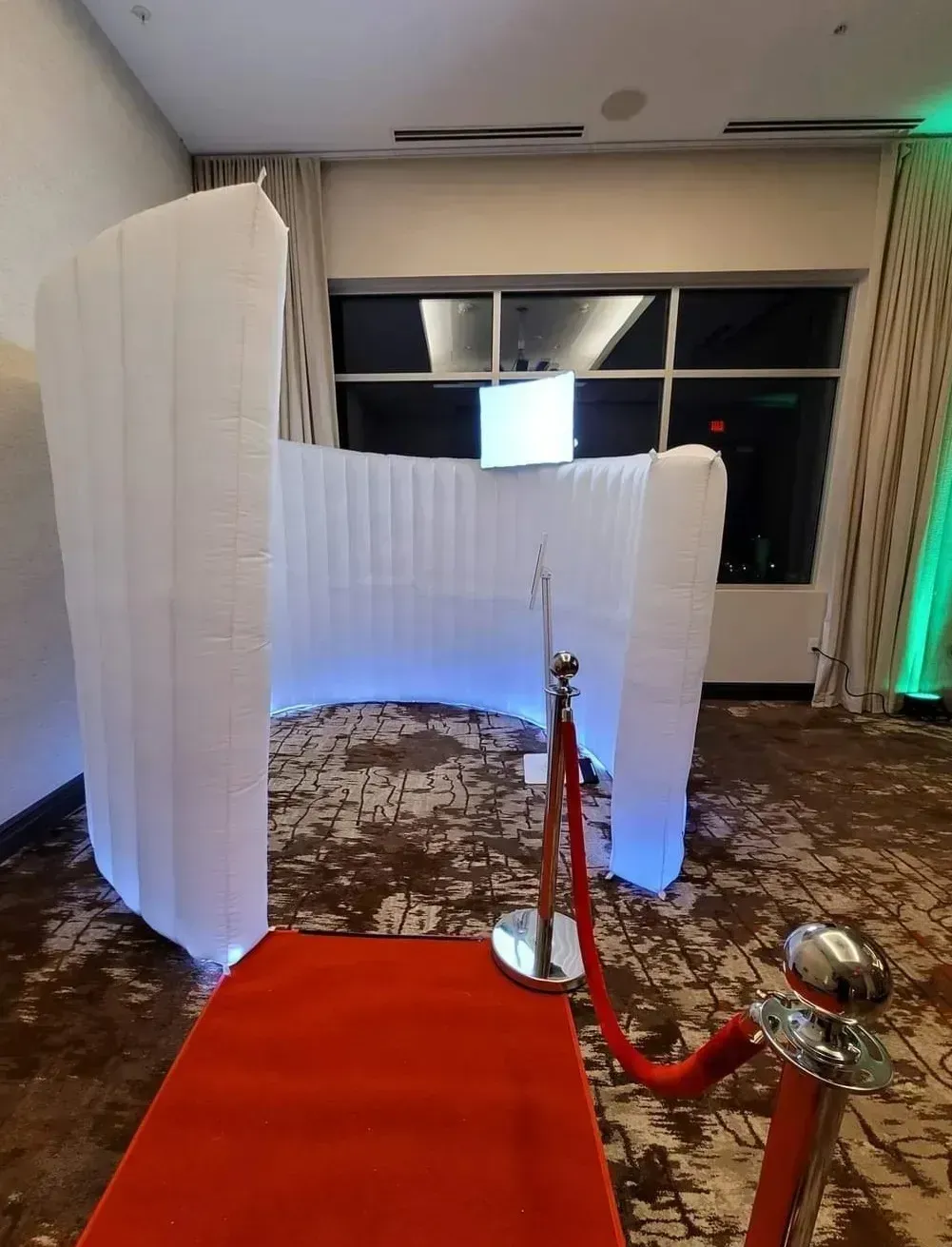 Red carpet leading to a white-lit abstract installation in a banquet hall with stanchions and curtains.