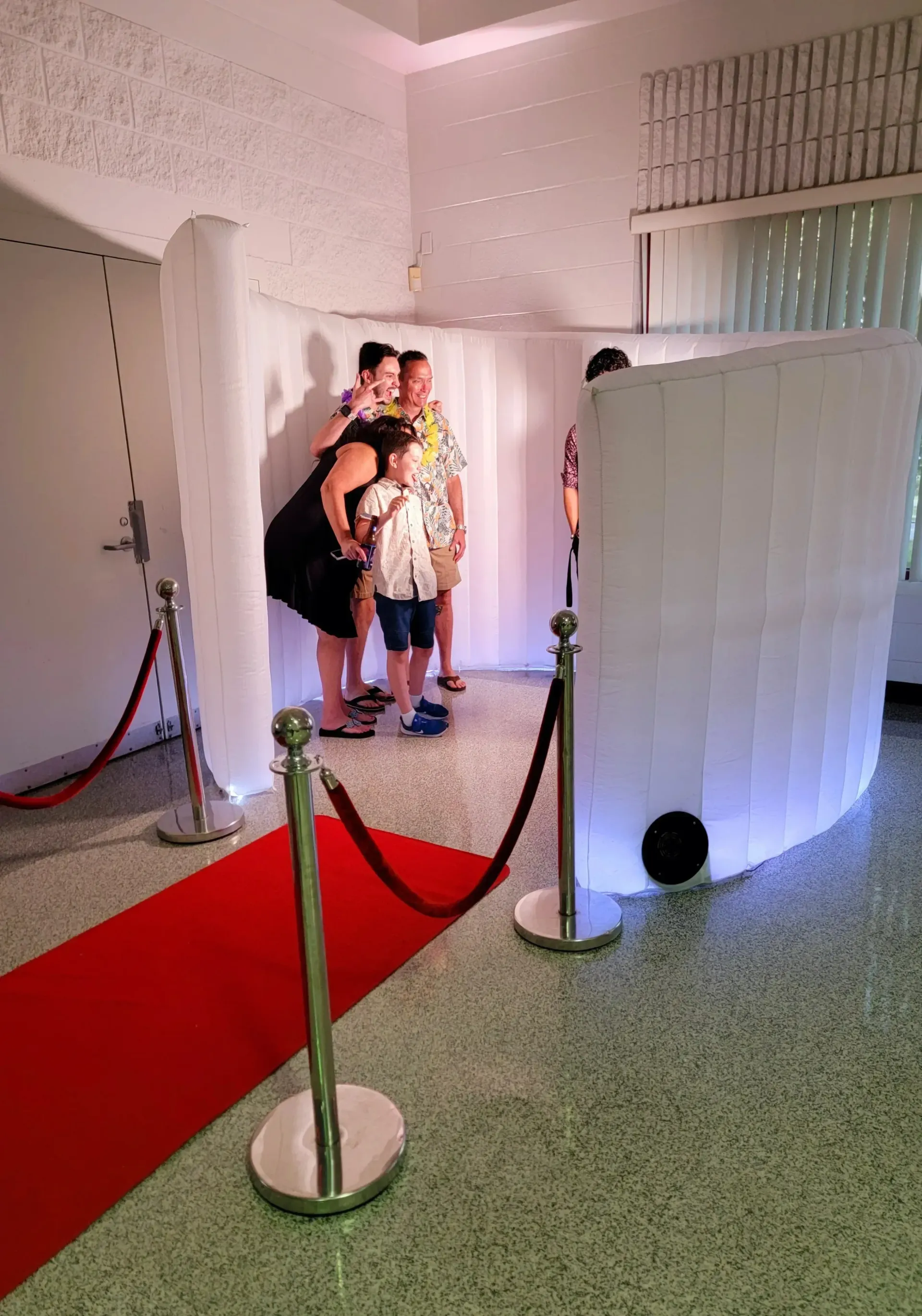 Three people stand by a red carpet in a bright room with white partition walls.