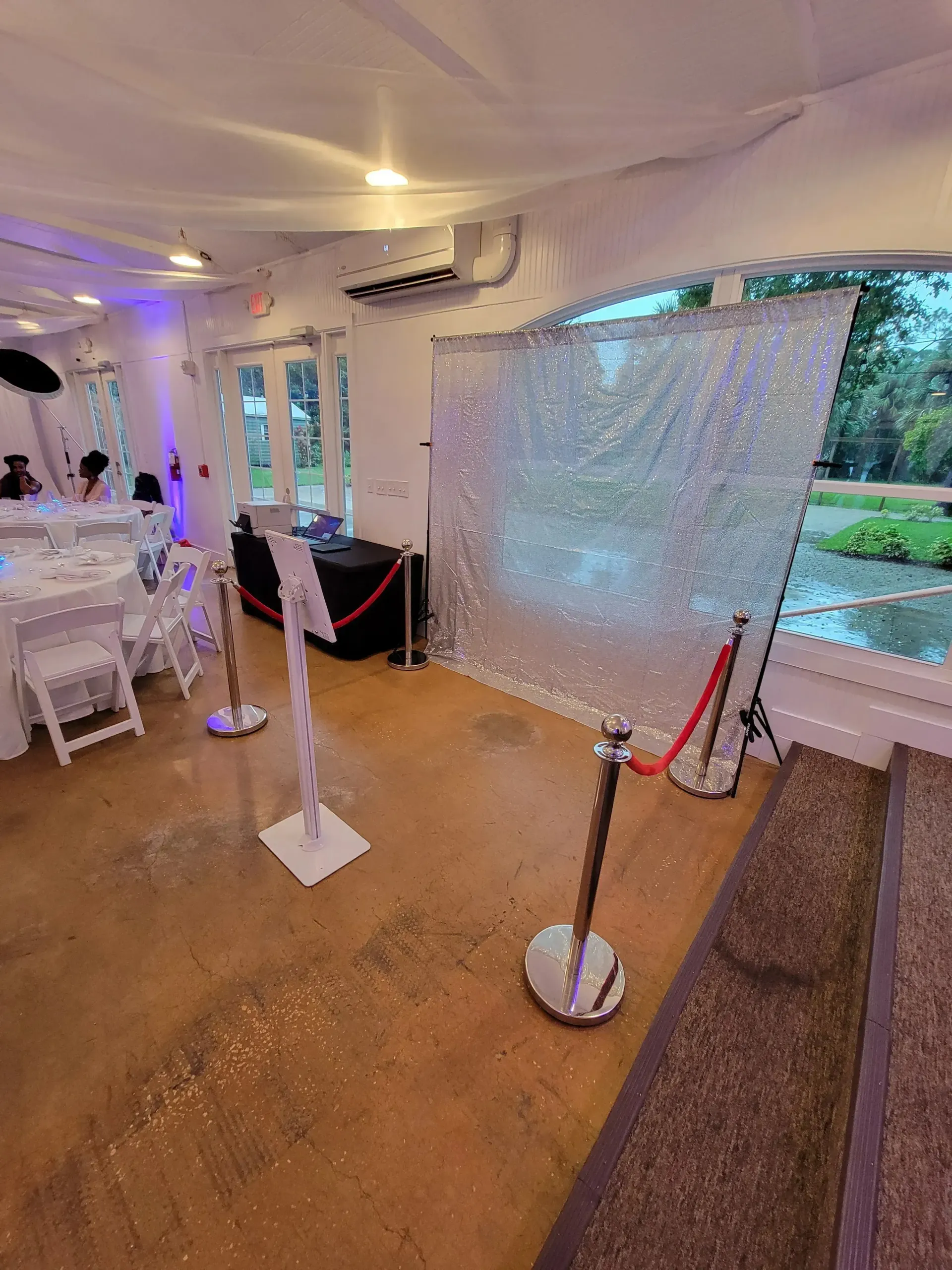Elegant indoor event tent with white drapes, sparkling backdrop, stanchions, and glass doors overlooking greenery