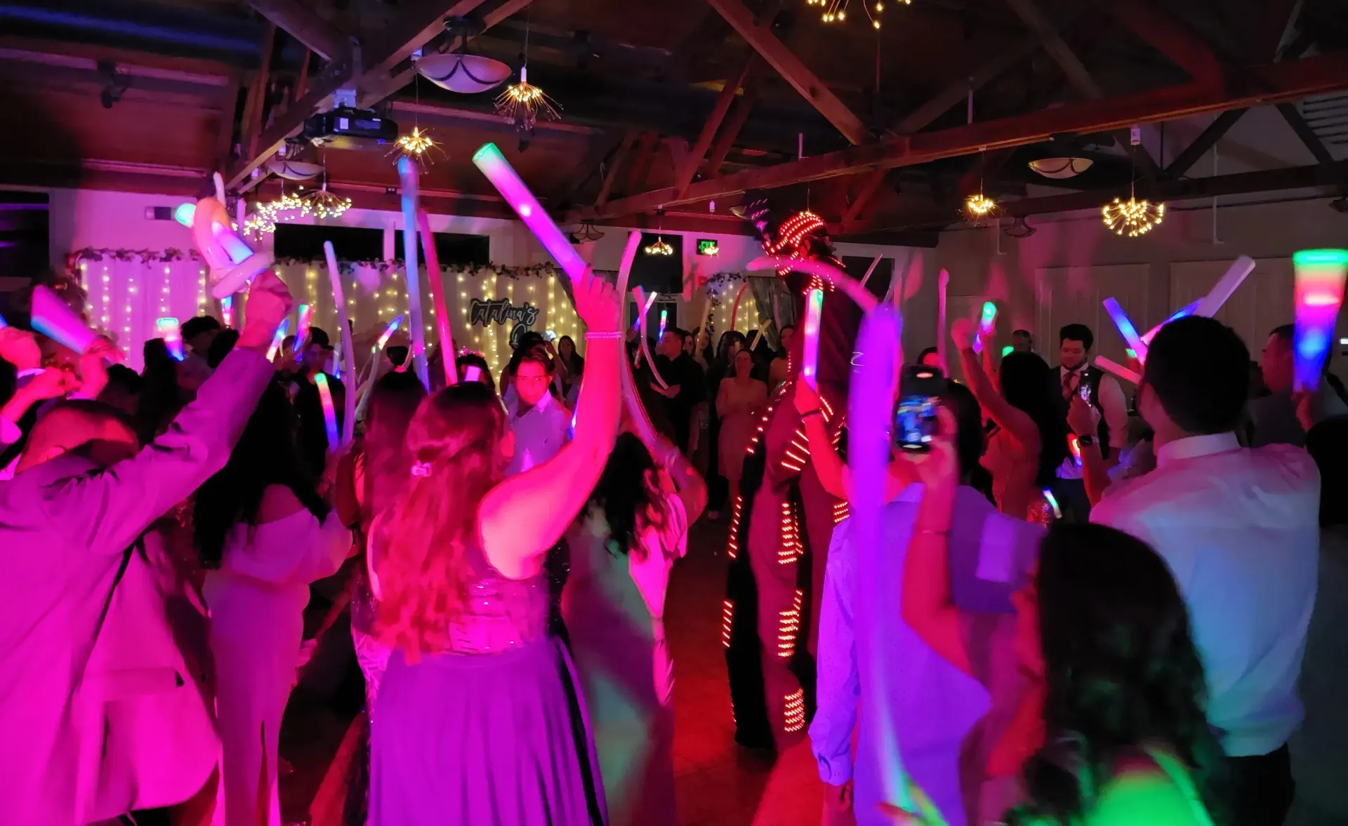 Crowd dancing at a neon-lit party with raised glow sticks under pink and purple lights