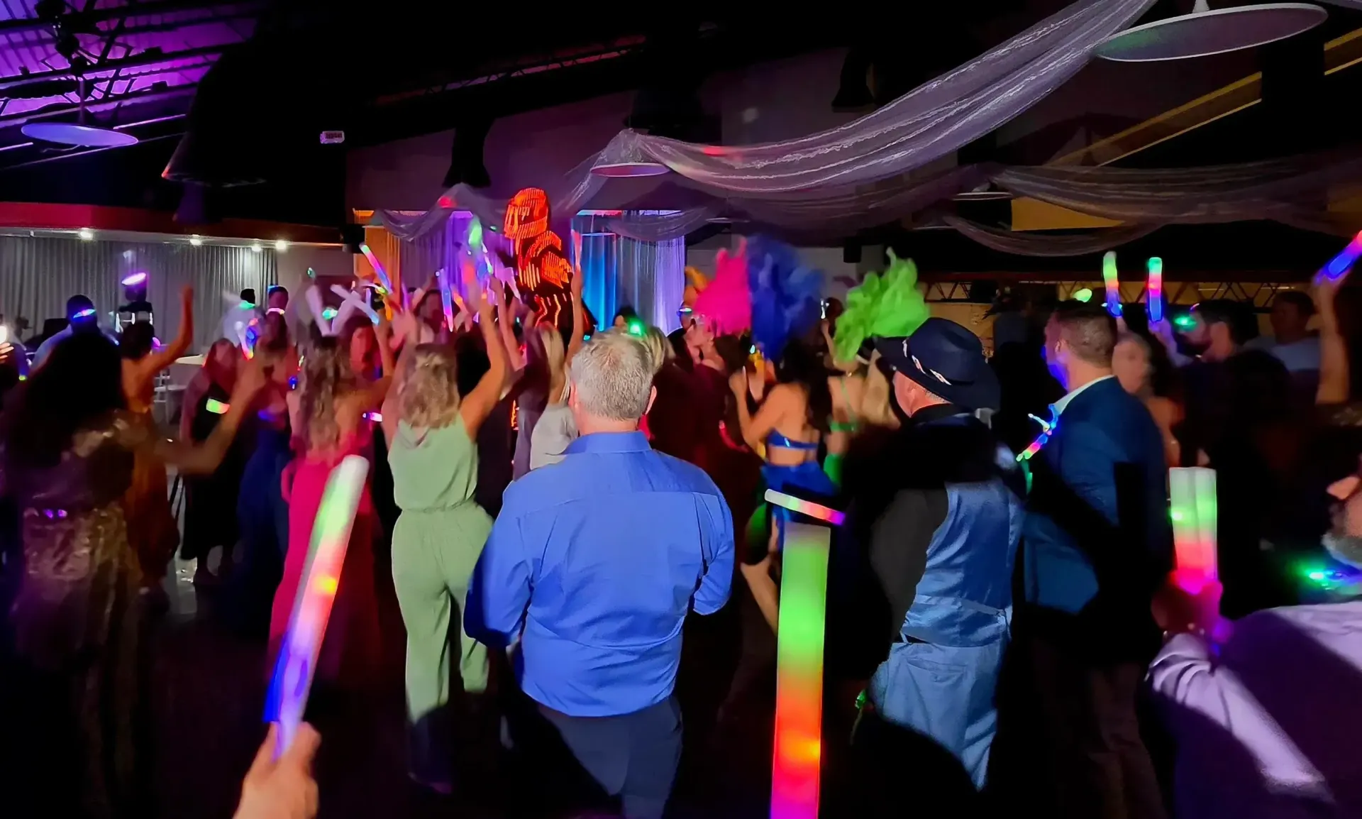 Crowd dancing at a colorful nightclub with neon glow sticks and performers on stage