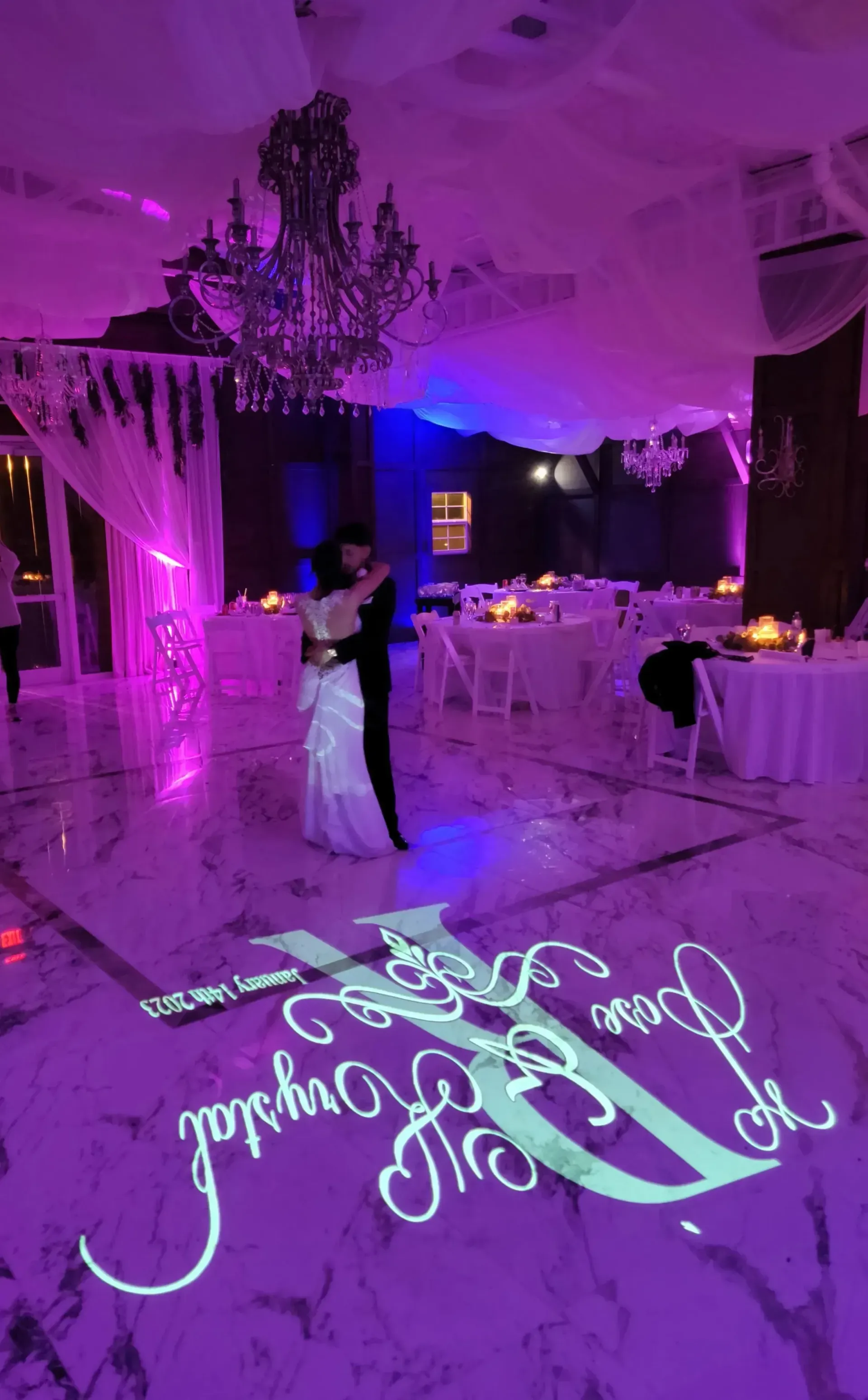 Couple dancing in a purple-lit wedding reception hall with mirrored monogram on the floor.