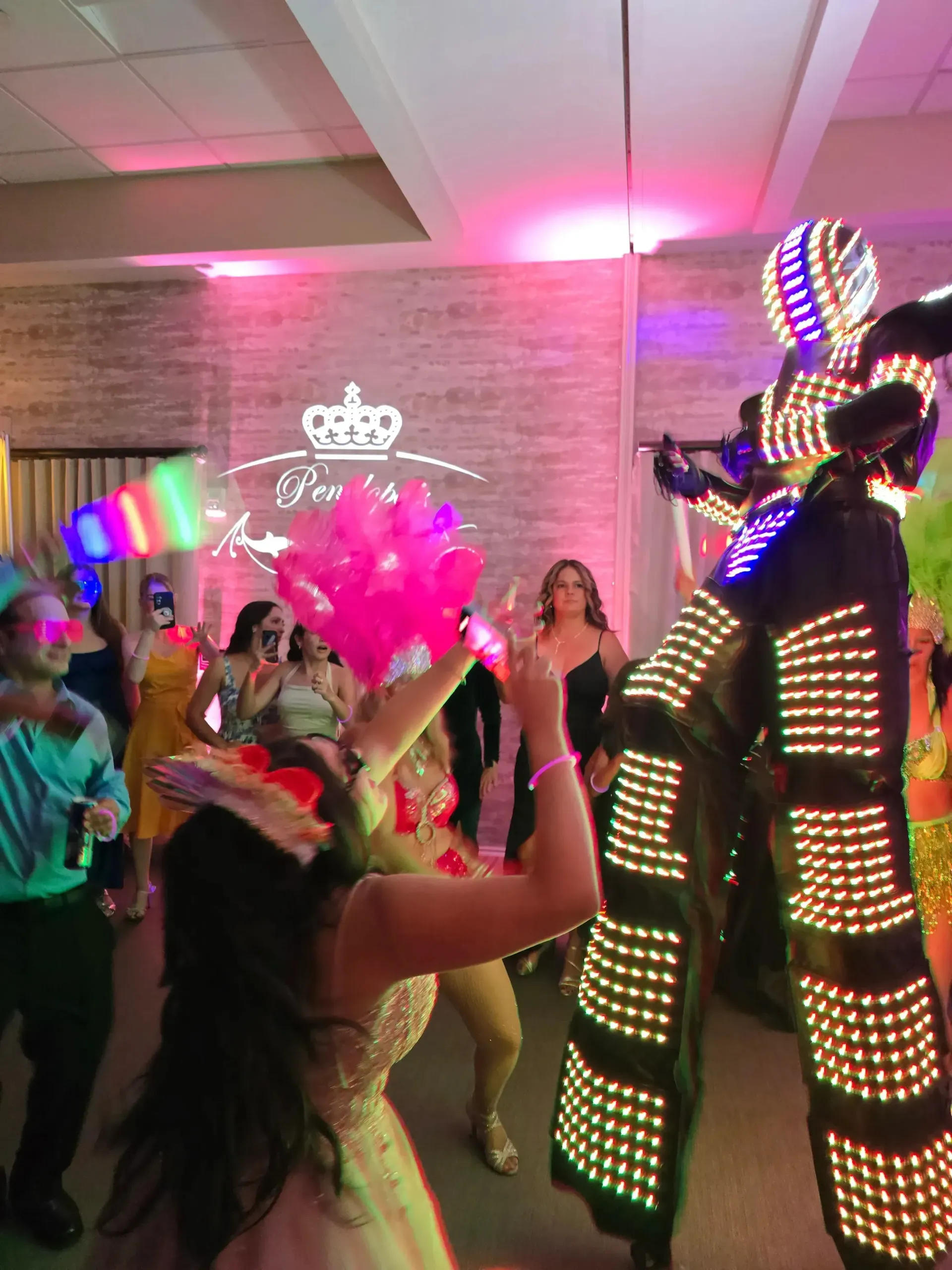 People dancing at a party, with bright pink and multicolored glowing costumes in a hall.