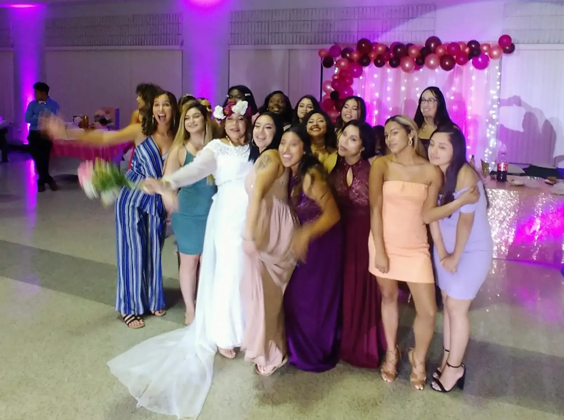 Group of women posing in dresses at a decorated indoor celebration with purple lights and balloons