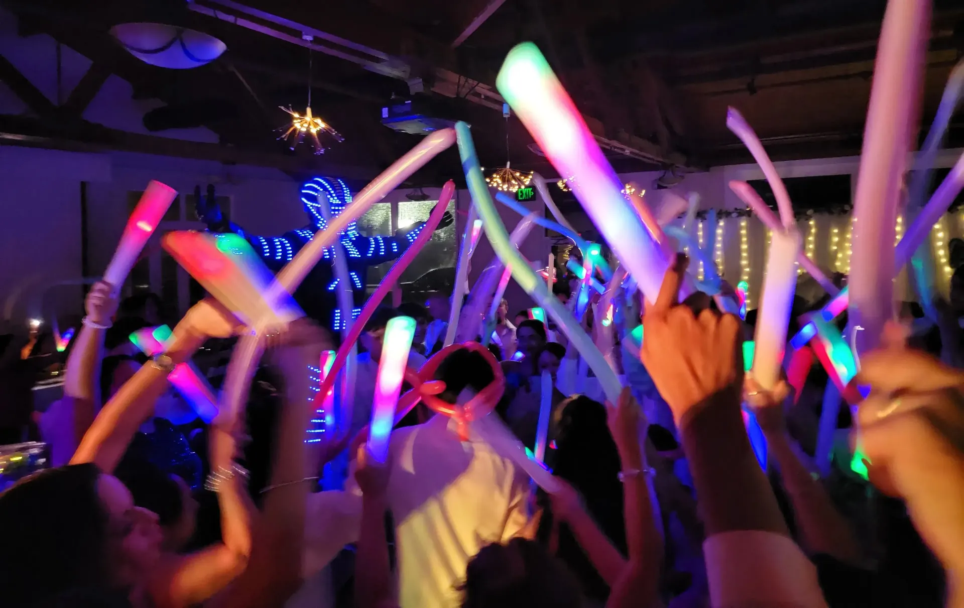 Crowd waving glowing neon light sticks at a lively indoor concert or party
