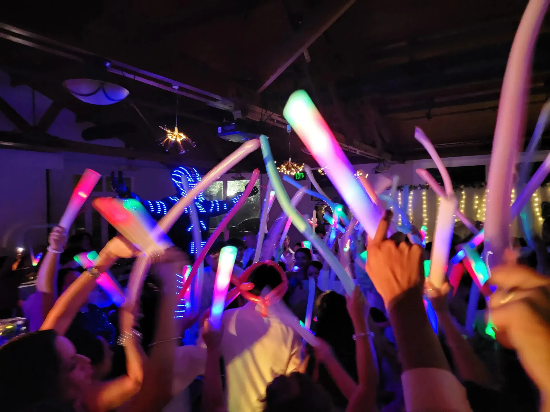 Crowd waving glowing neon light sticks at a lively indoor concert or dance event