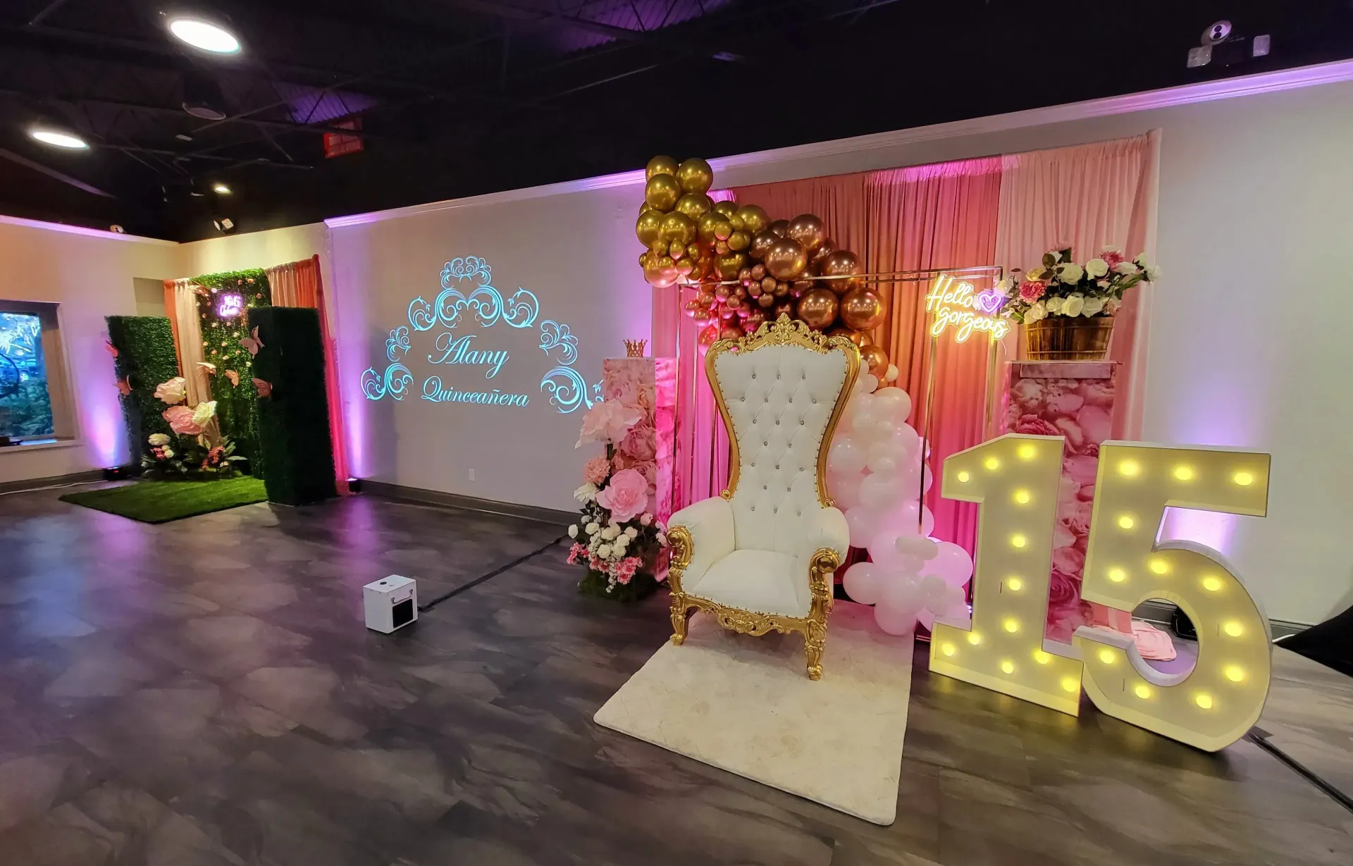 Decorated event stage with a white throne chair, pink floral backdrop, and lit “15” marquee numbers