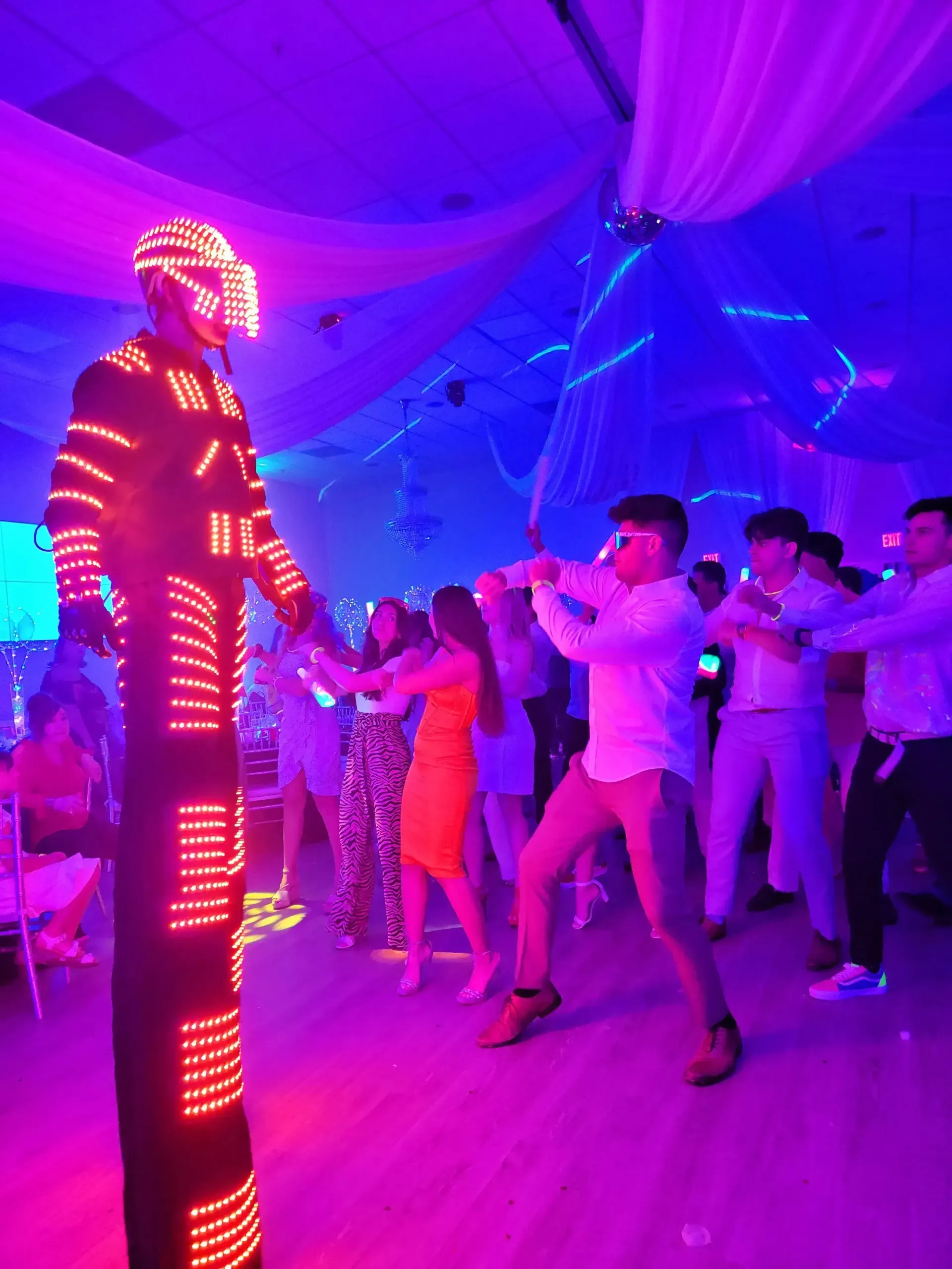 Party guests dancing with a neon-lit performer in a purple-lit event hall