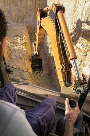 Man operating excavator Man operating a yellow excavator digging in a trench.