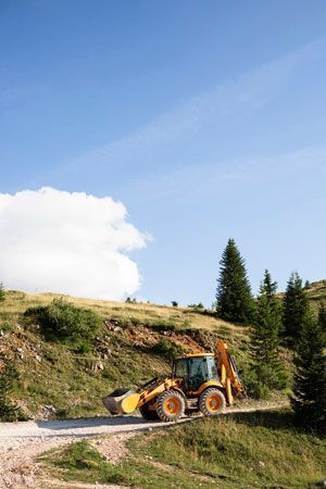 Yellow backhoe Yellow backhoe on a dirt road in a grassy hillside under a blue sky with a few clouds.