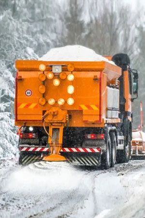 Orange snowplow truck Orange snowplow truck spreading salt on a snow-covered road in a wintery forest.