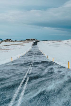 Road through snow-covered Road through snow-covered landscape with blowing snow, under a cloudy sky.