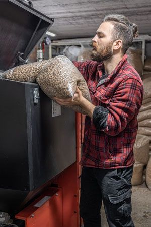 Man in red plaid shirt Man in red plaid shirt loading wood pellets into a heating unit; indoor setting.