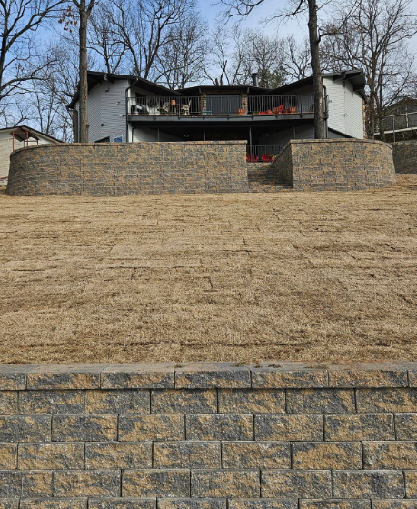 A house is sitting on top of a hill next to a brick wall.