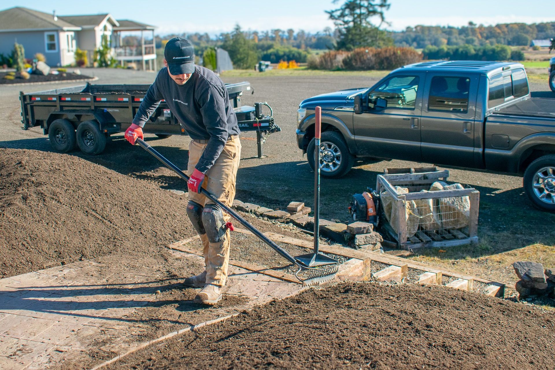 Worker leveling dirt beside a black pickup truck at a residential construction site