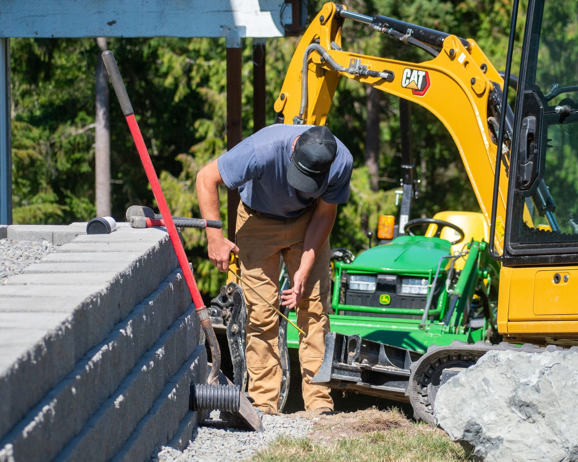 Worker shoveling beside a yellow excavator at a roadside construction site