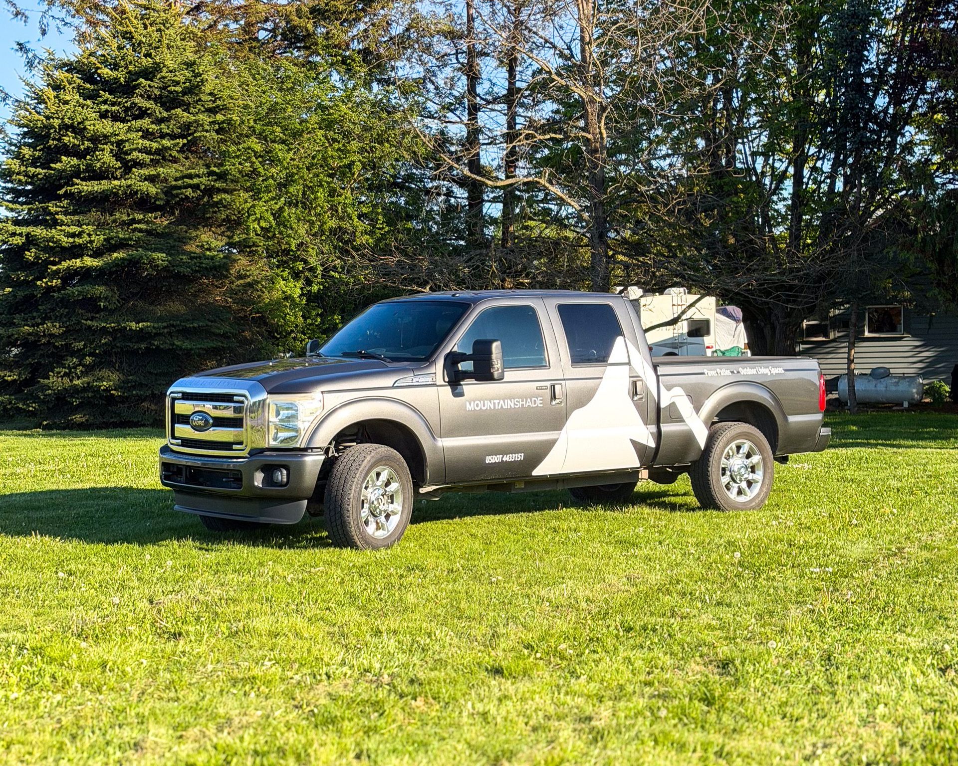 Gray pickup truck parked on grass with driver door open, near trees on a sunny day