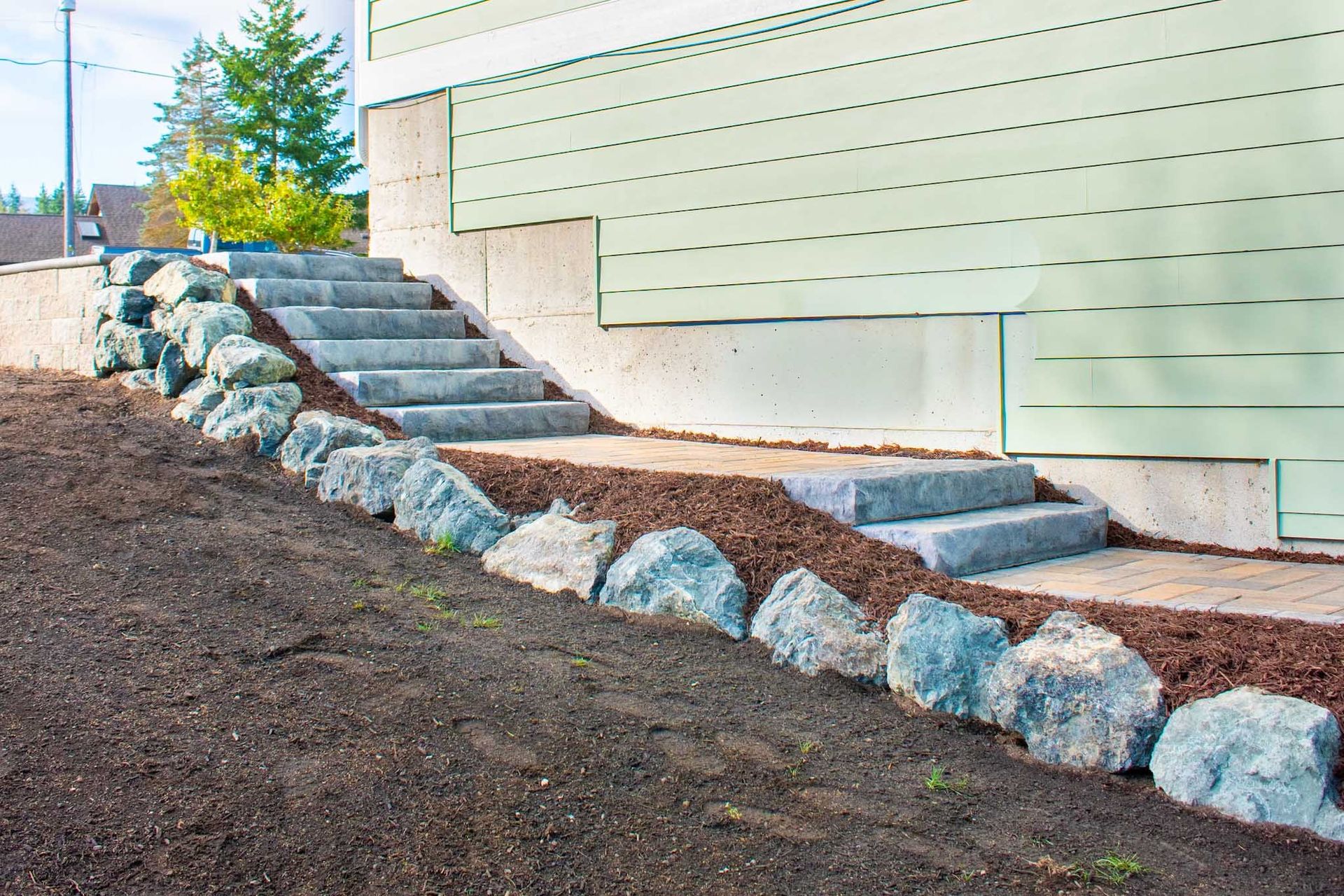 Stone steps lead to a light green building. Large rocks line the steps with mulch around them.