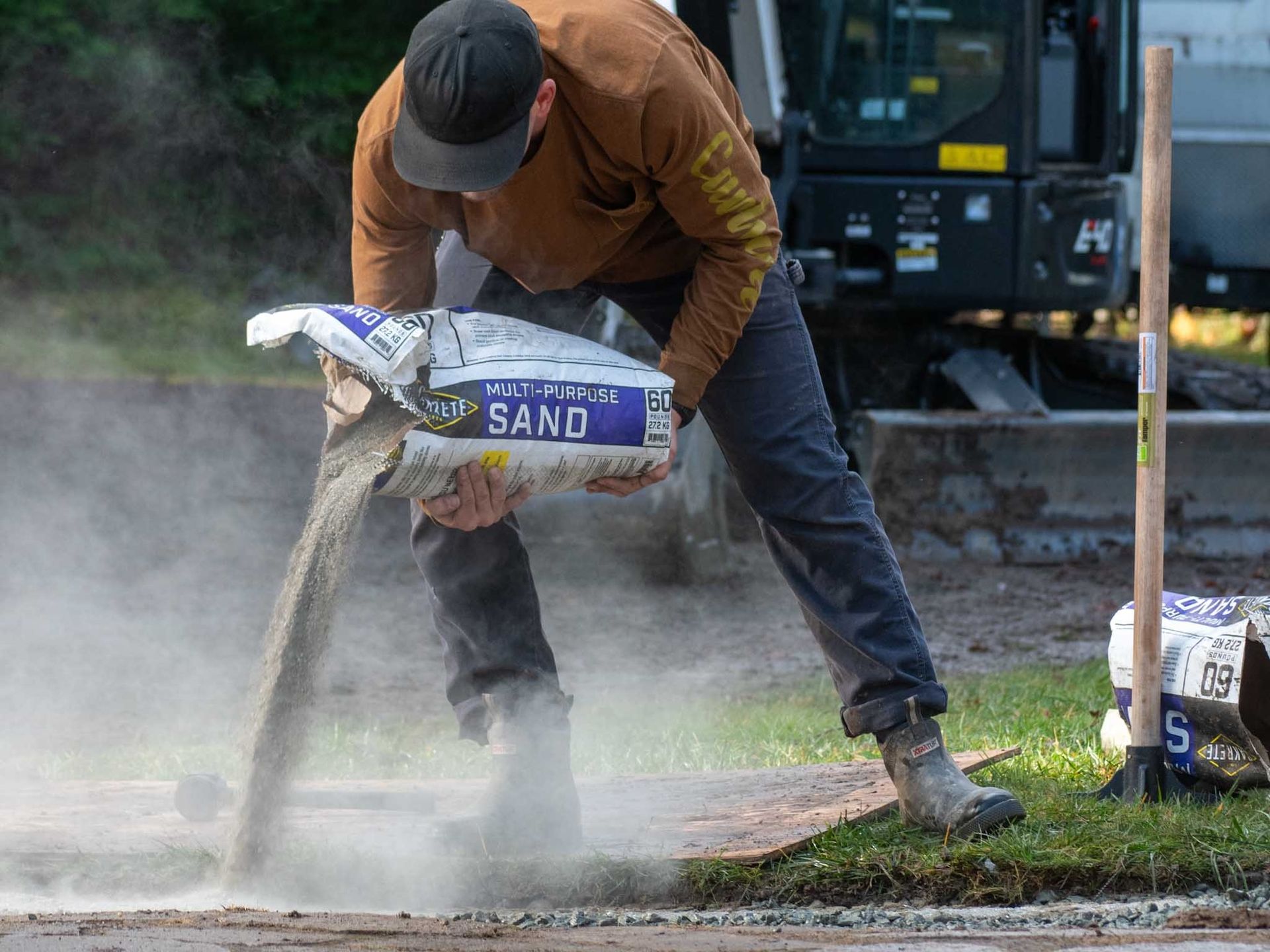 Man in work clothes pouring sand from a bag onto a road. Construction scene.