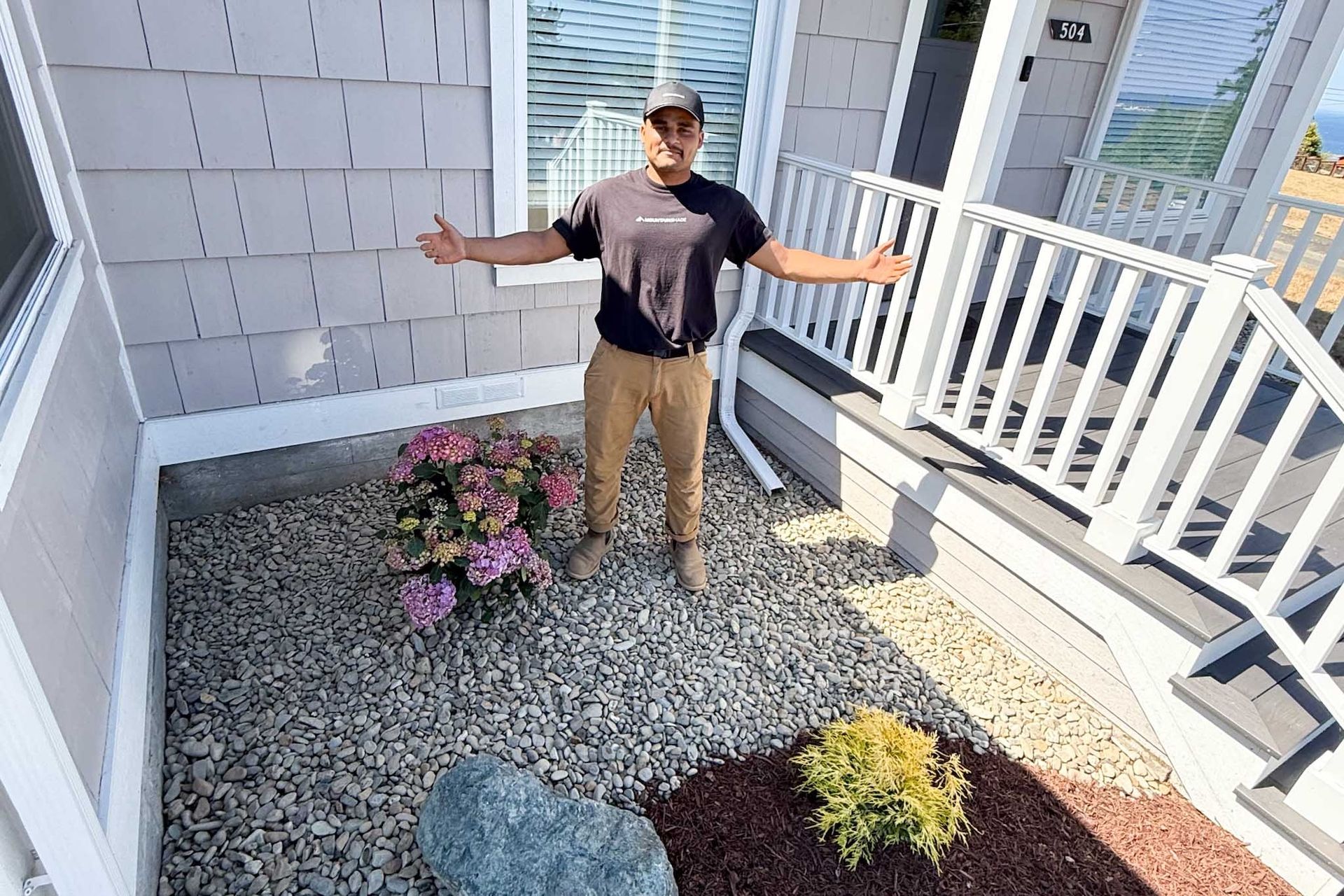 Man standing in a gravel-covered area in front of a house, arms outstretched.