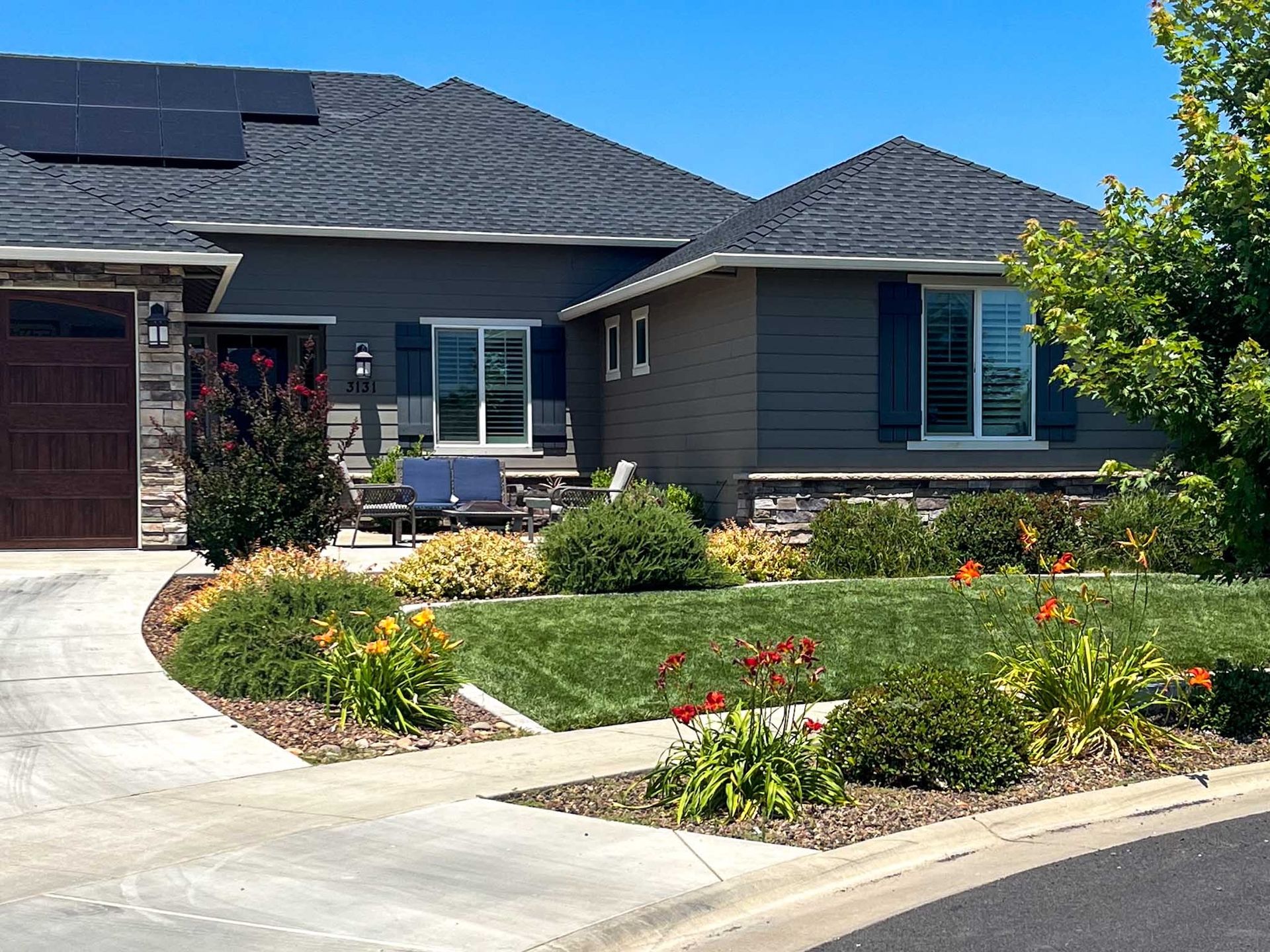 Gray house with solar panels, blue shutters, and a well-manicured lawn.