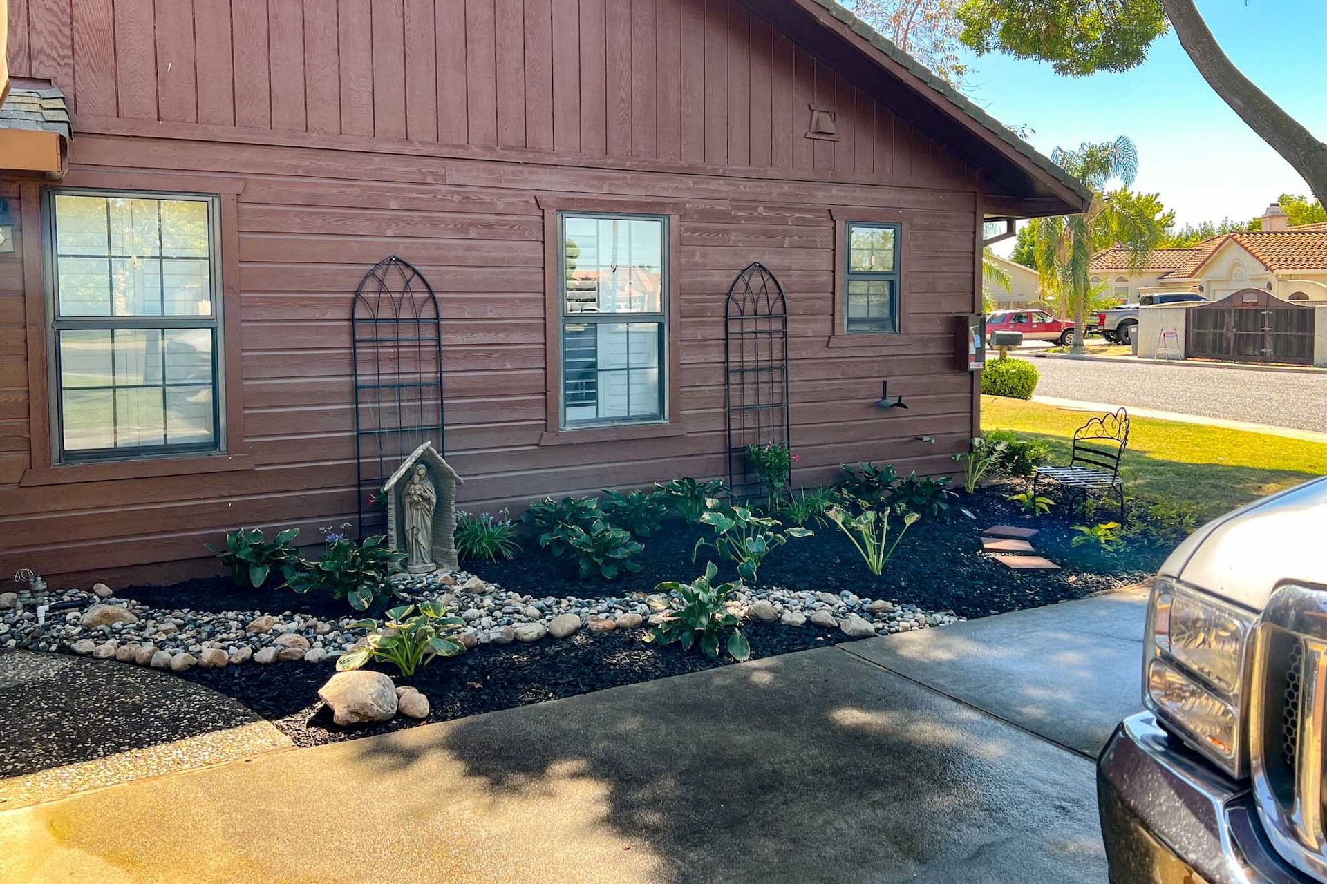 Brown house with a newly landscaped front yard, a statue, and decorative metal trellises.