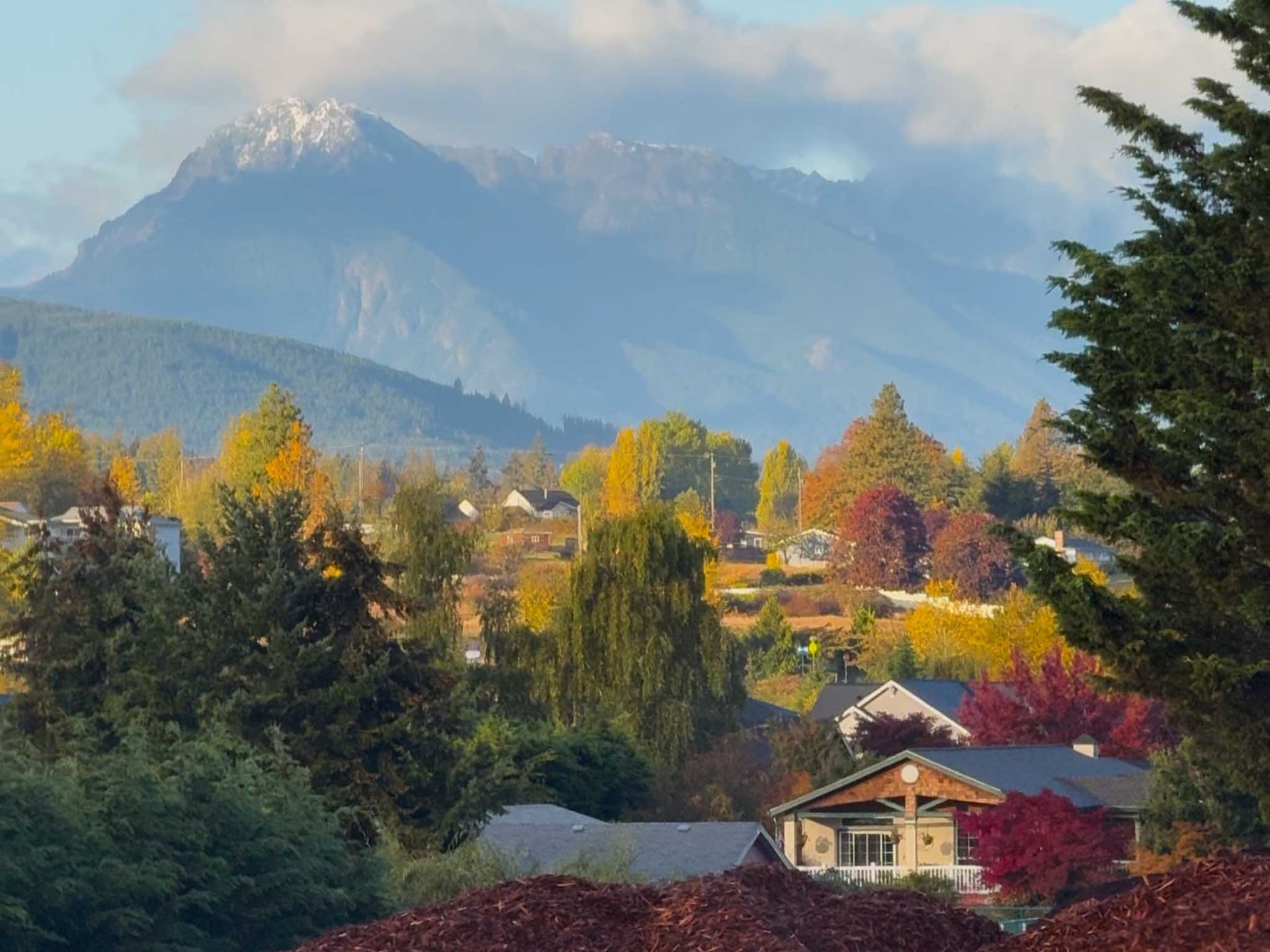 Autumn landscape: houses nestled among colorful trees, snow-capped mountain backdrop.