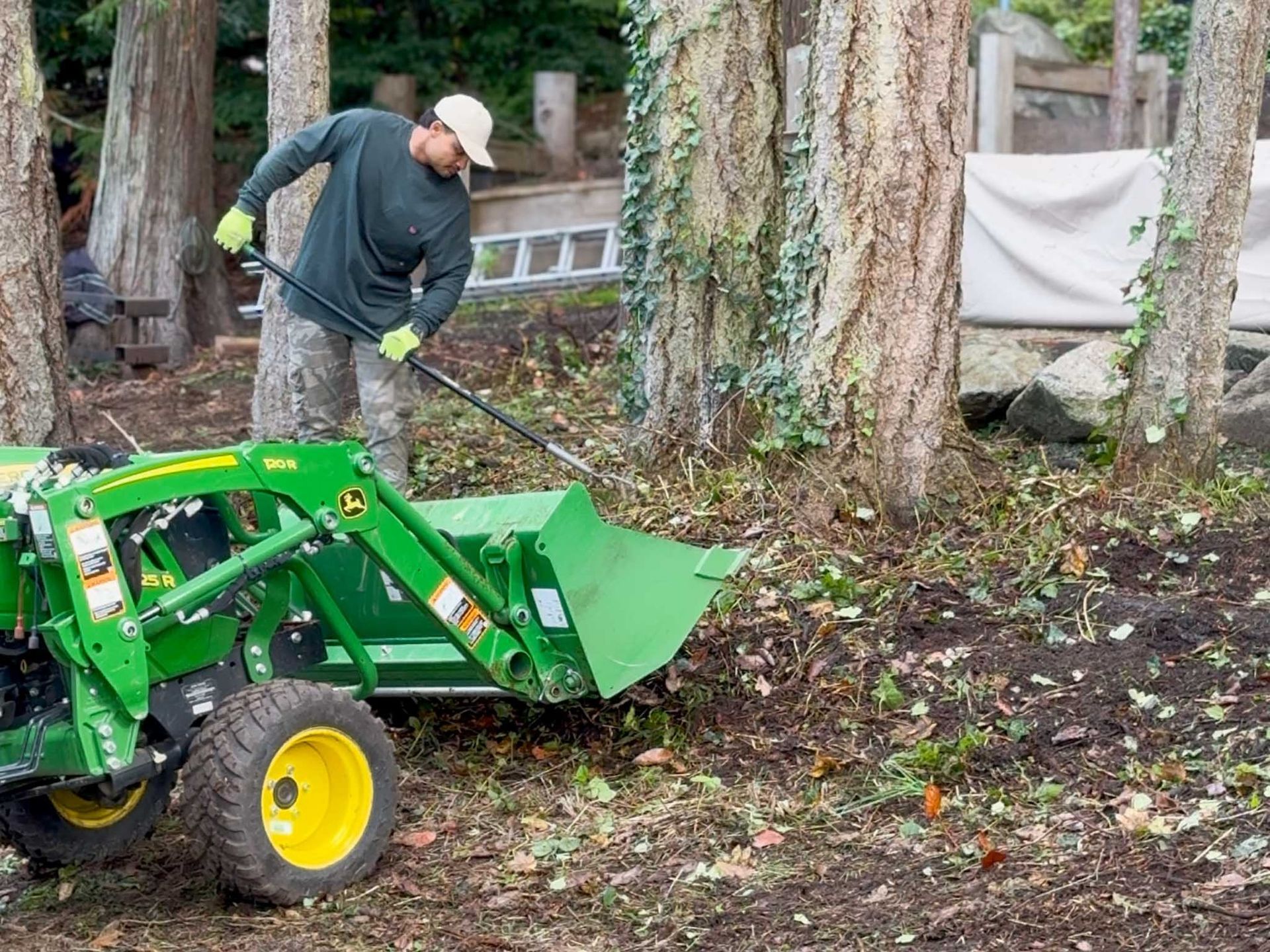 Man using a John Deere tractor and loader to move debris near trees.