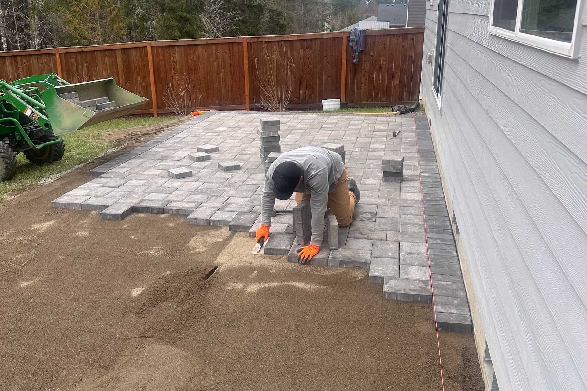 Person installing paving stones in a backyard next to a house.