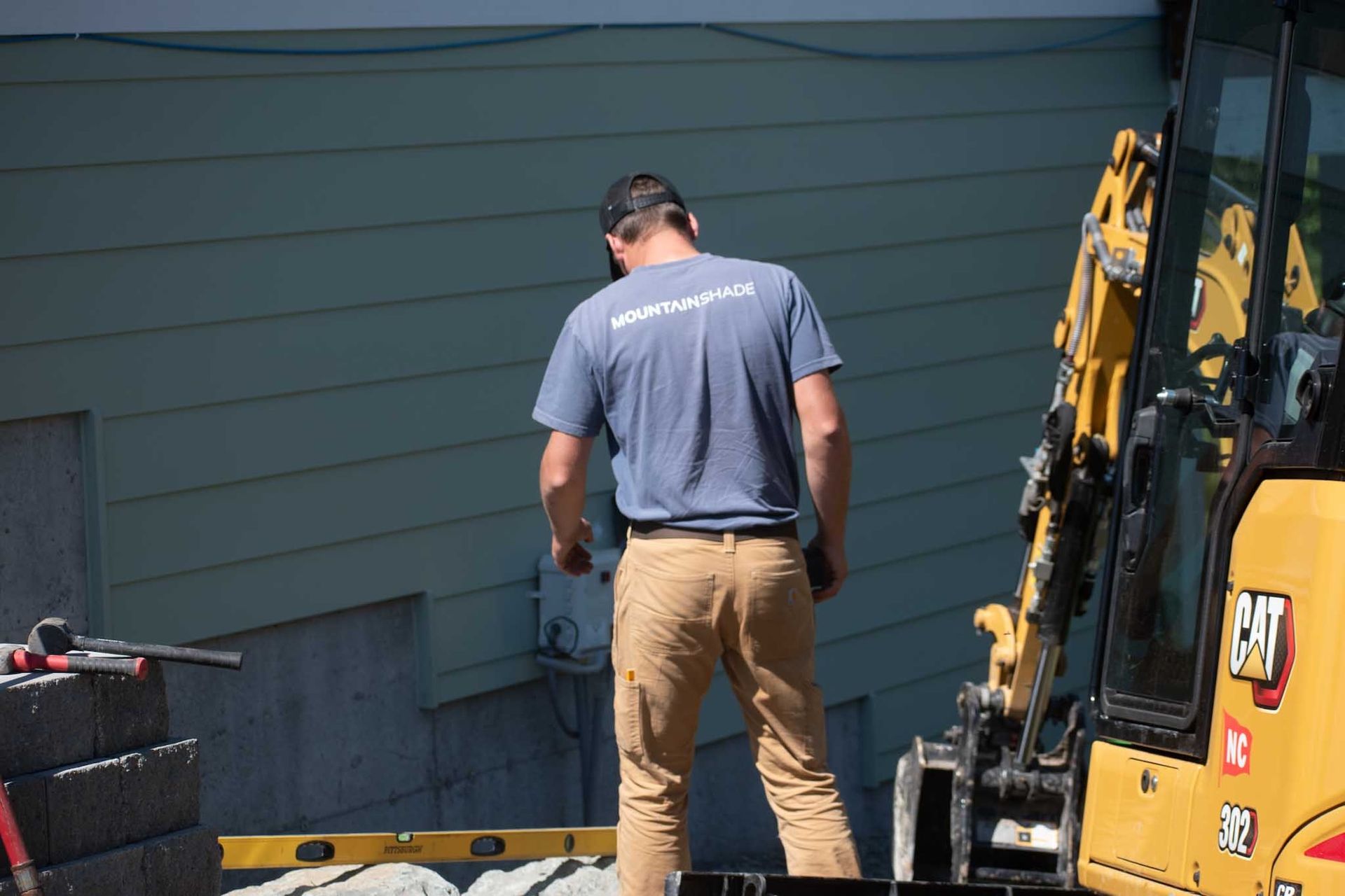 A man in work clothes stands near a yellow excavator, working on a construction site.