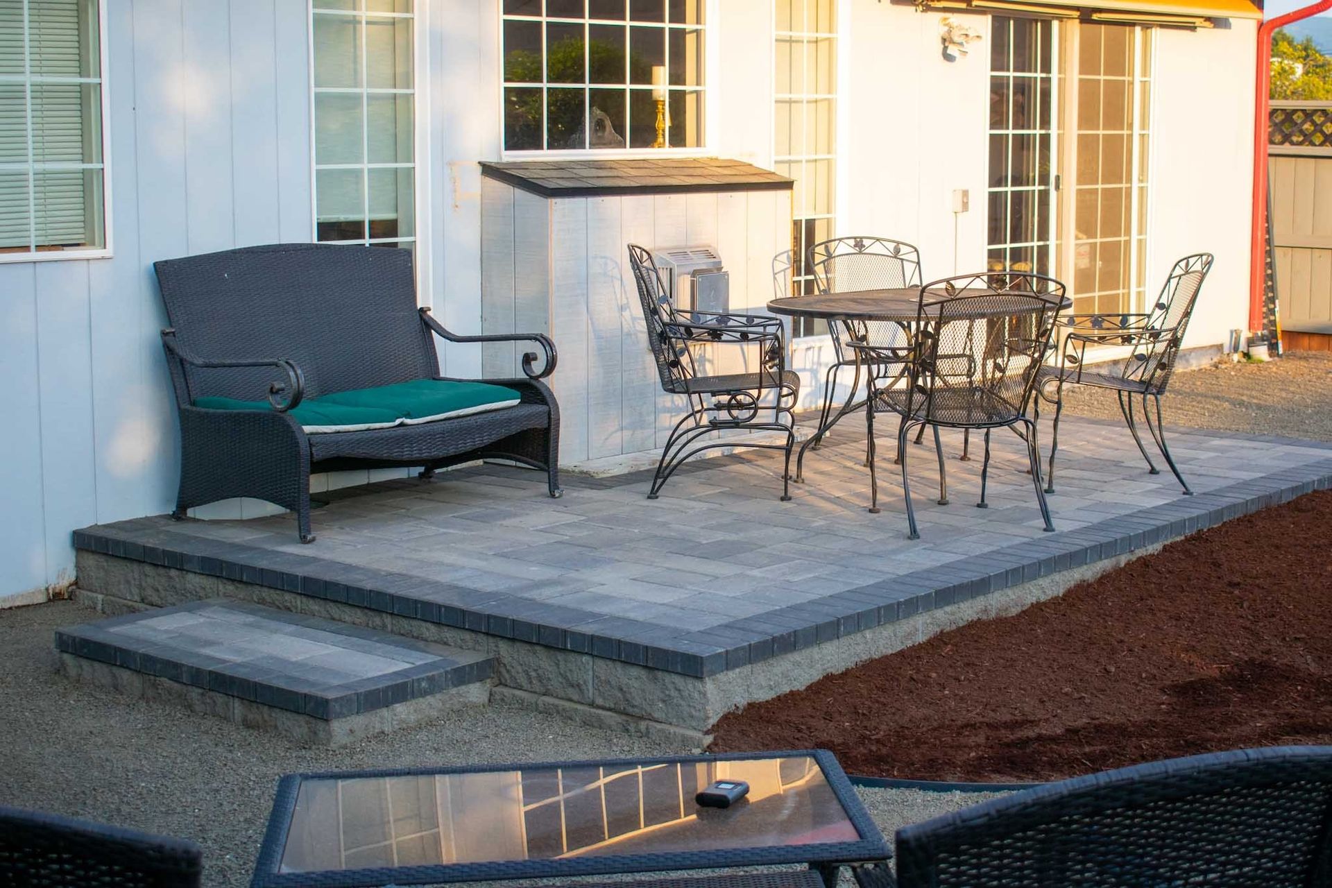 Patio with seating, steps, and a dining table against a white house.