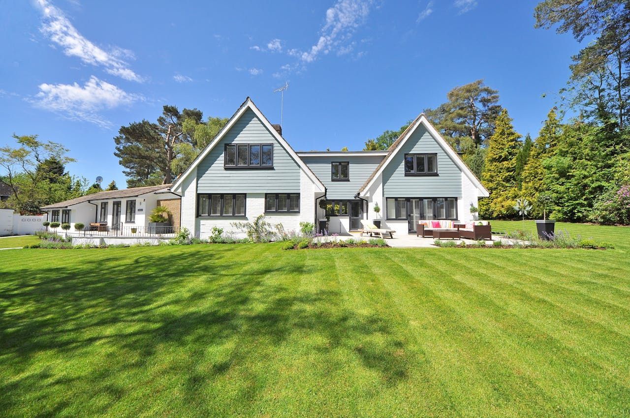 Two-story white house with blue accents, set on a lush green lawn on a sunny day.
