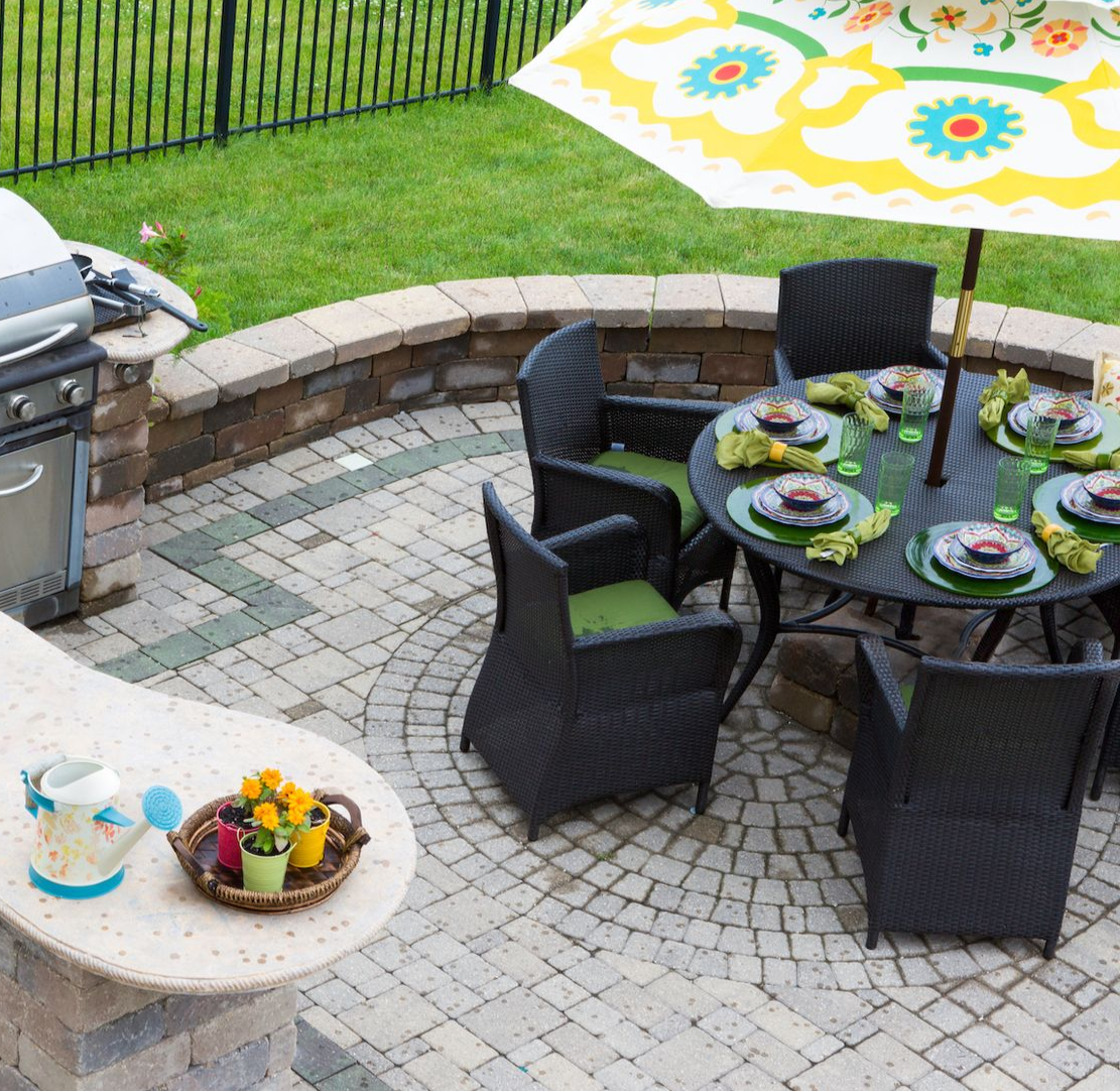 Patio with round table, chairs, umbrella, grill, and counter, set for a meal.