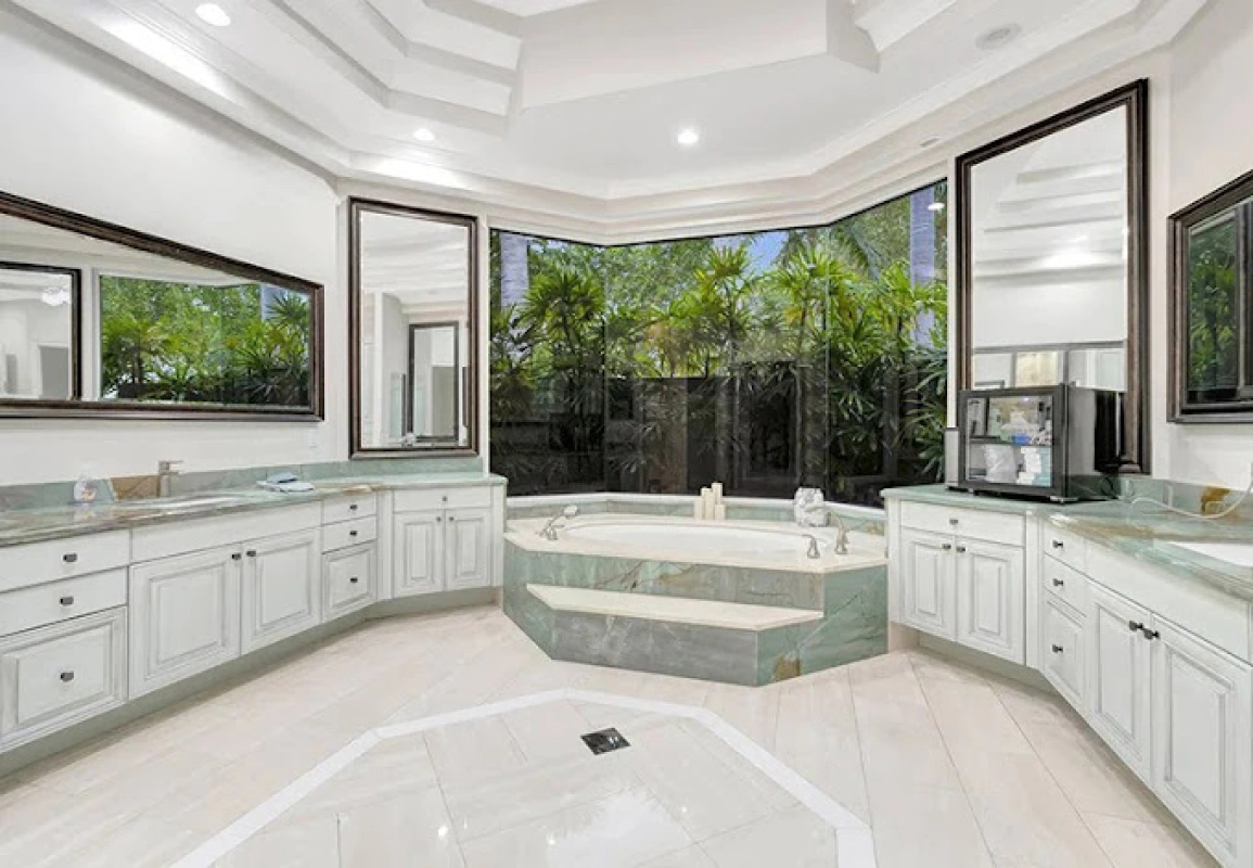 Luxurious bathroom with white cabinets, jacuzzi, large windows, and two mirrors.