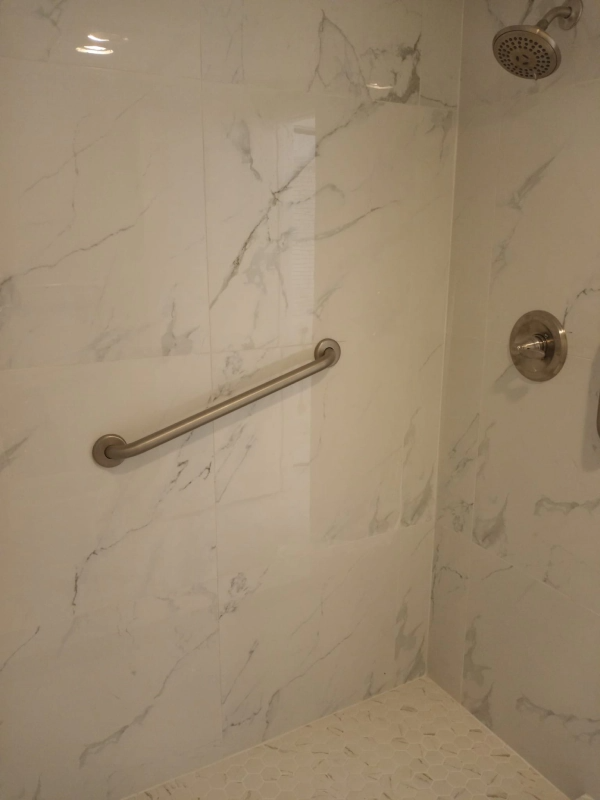 Shower stall with marble-look tile, a grab bar, showerhead, and faucet.