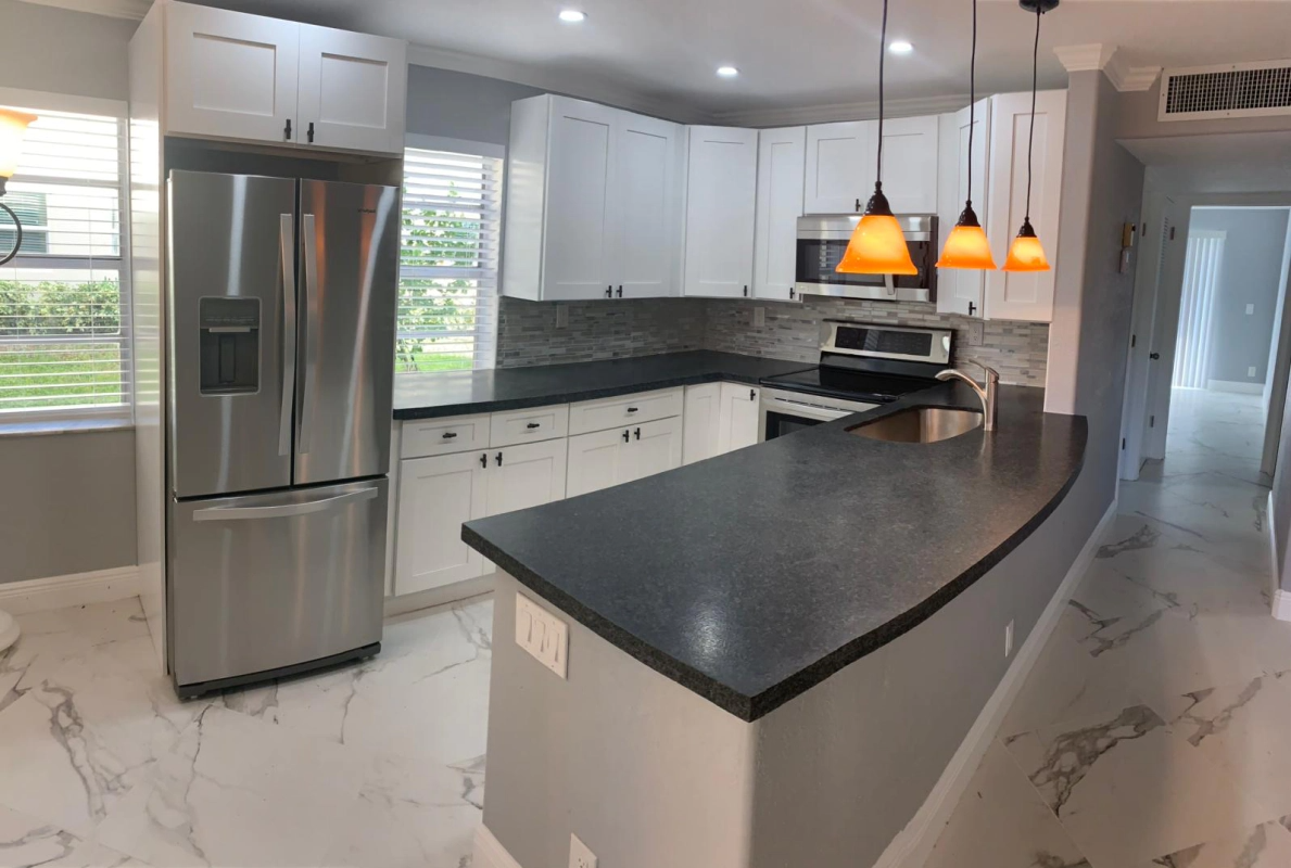 Modern white kitchen with stainless steel appliances and black countertops.