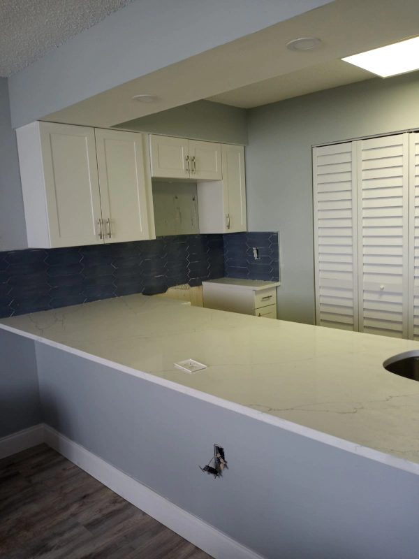 Kitchen with white cabinets, light countertops, blue backsplash, and shuttered door.